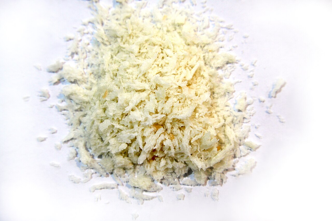 Close-up photograph of pale, irregular panko breadcrumb flakes on a white surface.