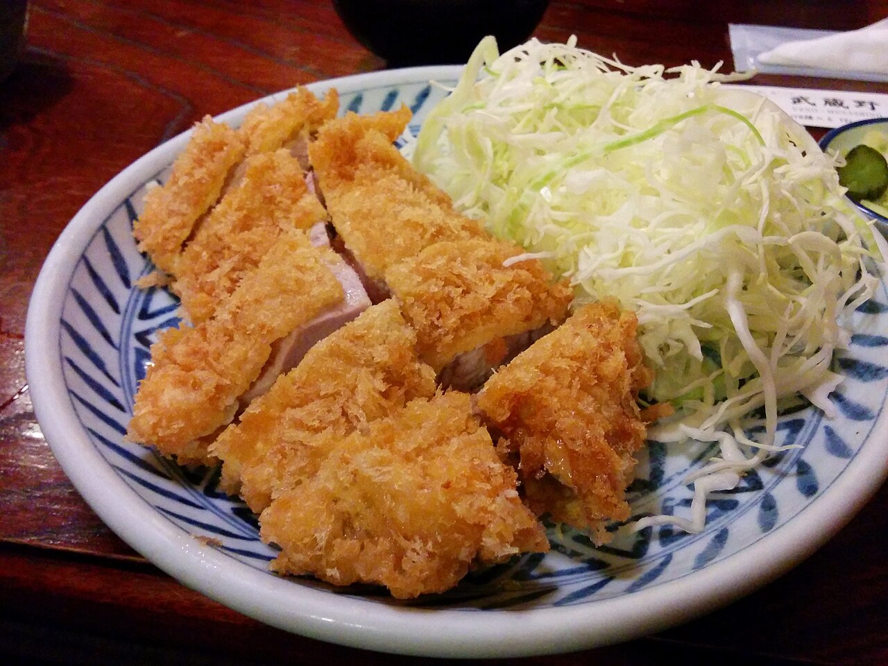 A sliced breaded pork cutlet with a golden crumb coating served beside shredded cabbage.